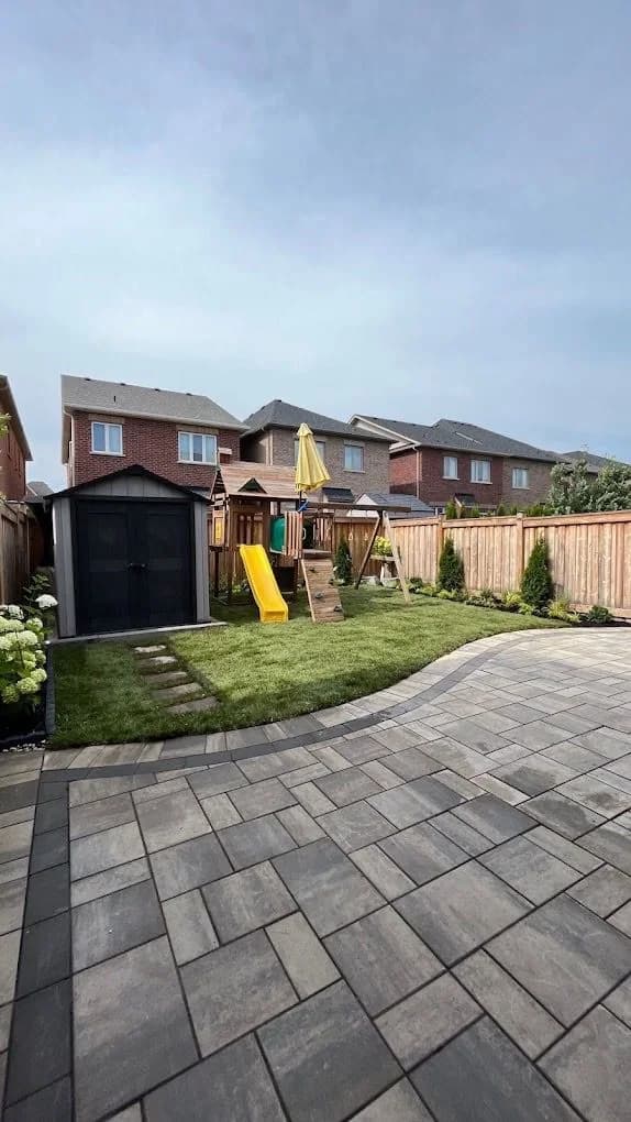 Family backyard with fresh sod, planting beds, and a curved paver patio