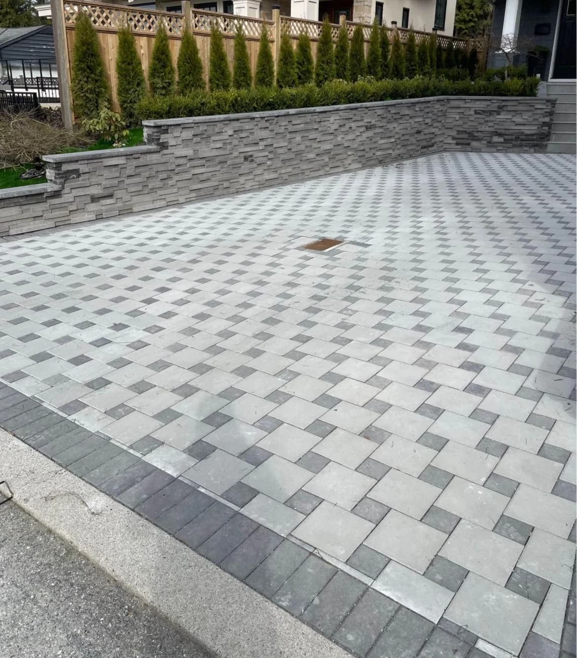 Patterned paver driveway meeting a raised stone planting wall