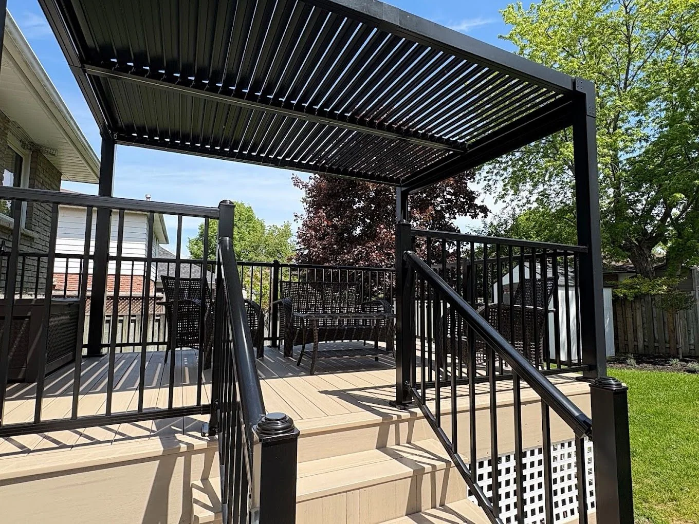 Raised deck and black louvered pergola surrounded by lawn