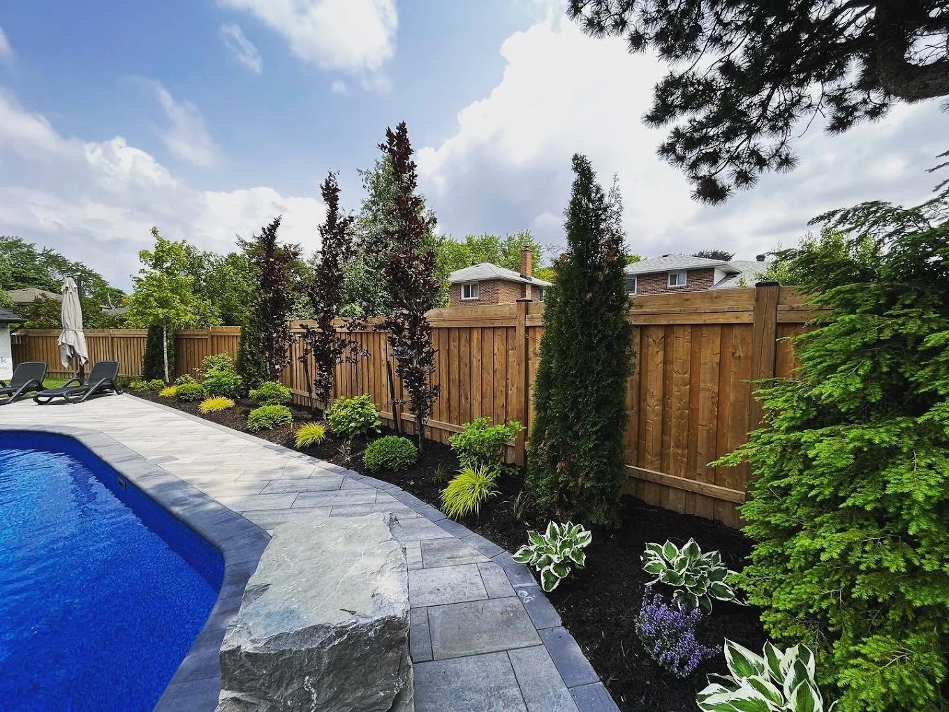 Poolside stonework and layered evergreen planting along a privacy fence