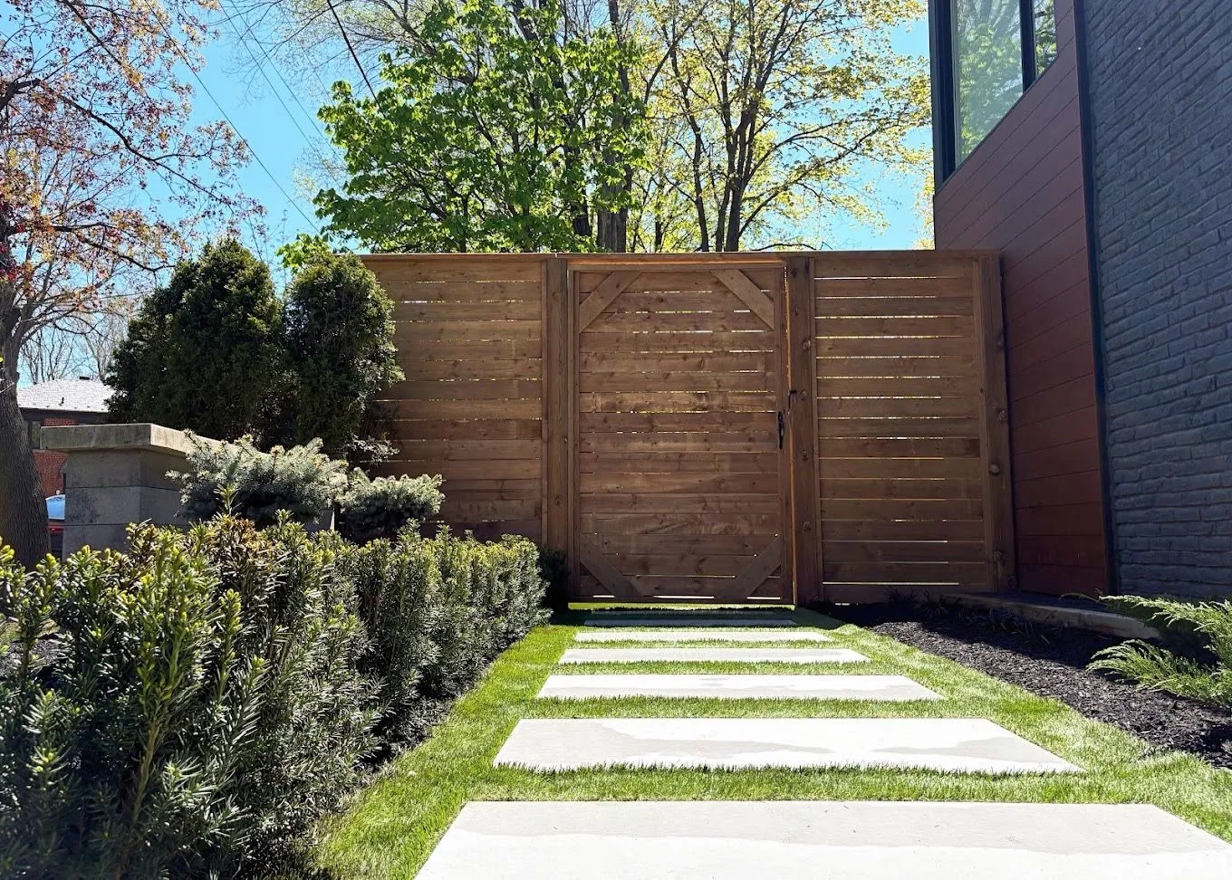 Large-format stepping stones set through lawn toward a horizontal cedar gate