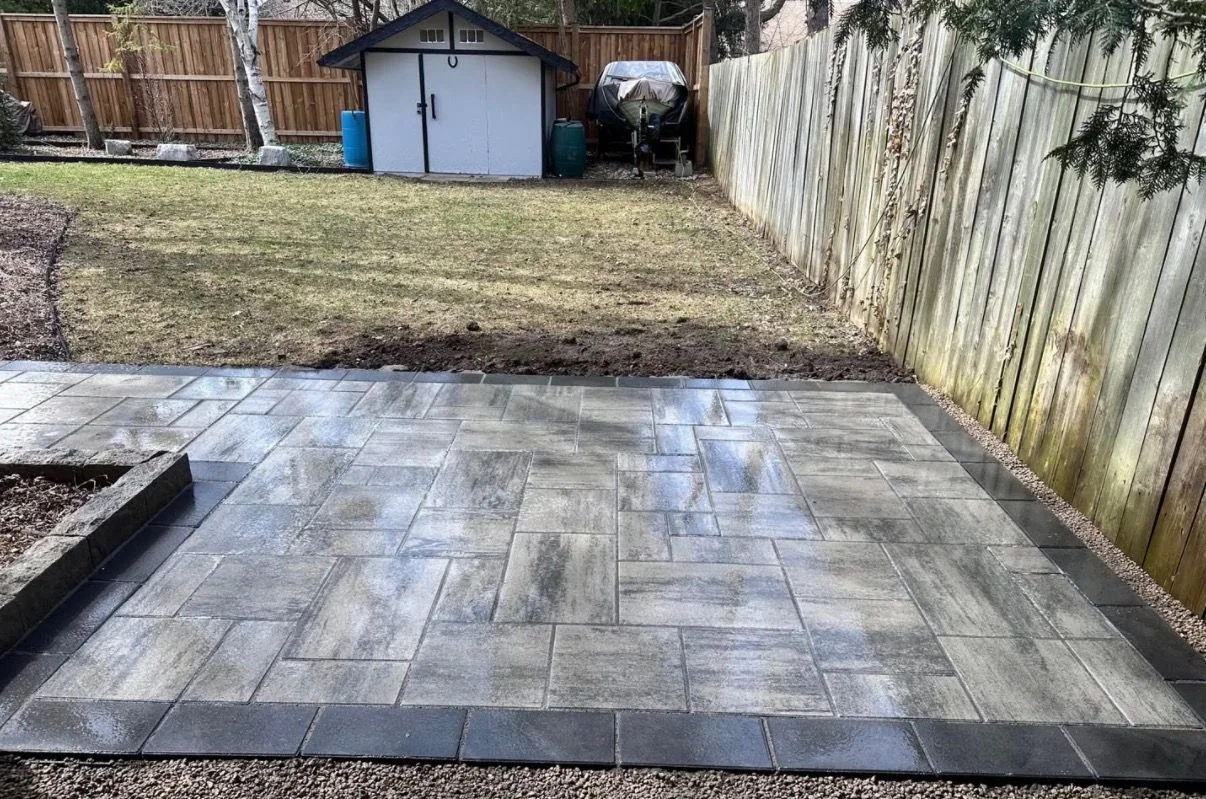 Finished rectangular paver patio with dark border beside a mature yard