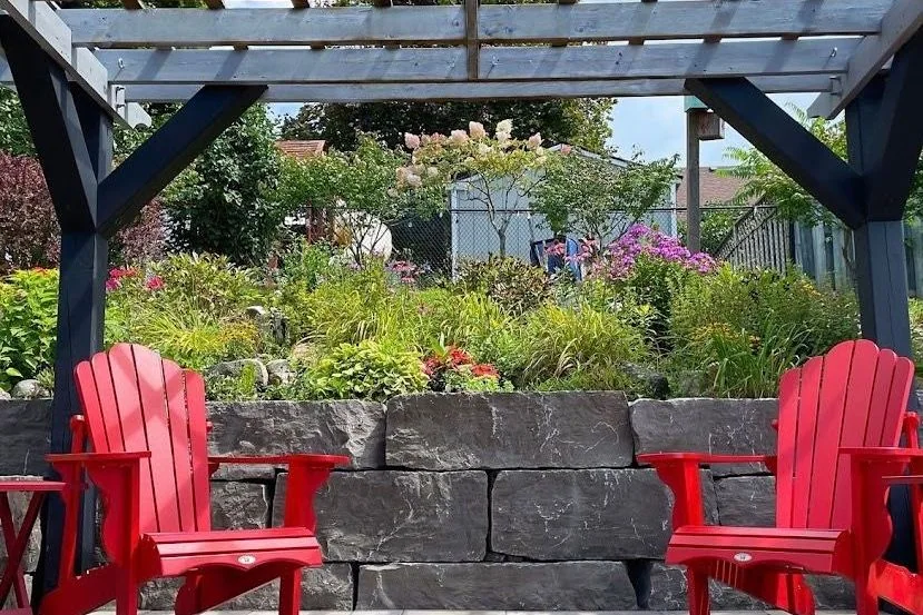 Pergola seating area backed by a natural stone retaining wall and flowers