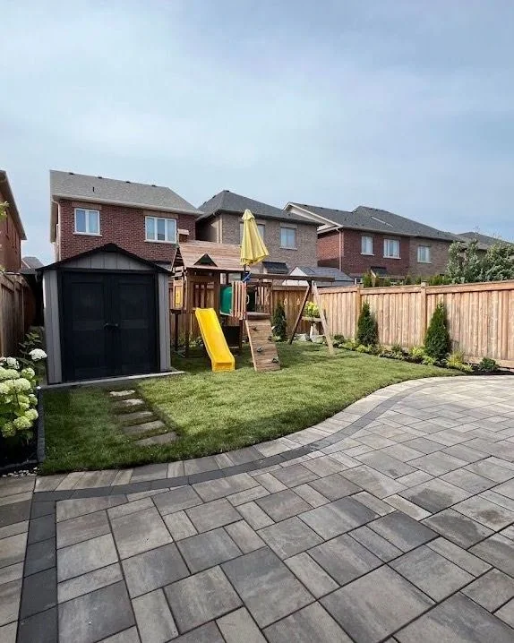 Family backyard with fresh sod, planting beds, and a curved paver patio