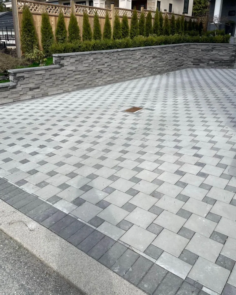 Patterned paver driveway meeting a raised stone planting wall